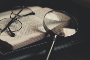 gray magnifying glass and eyeglasses on top of open book