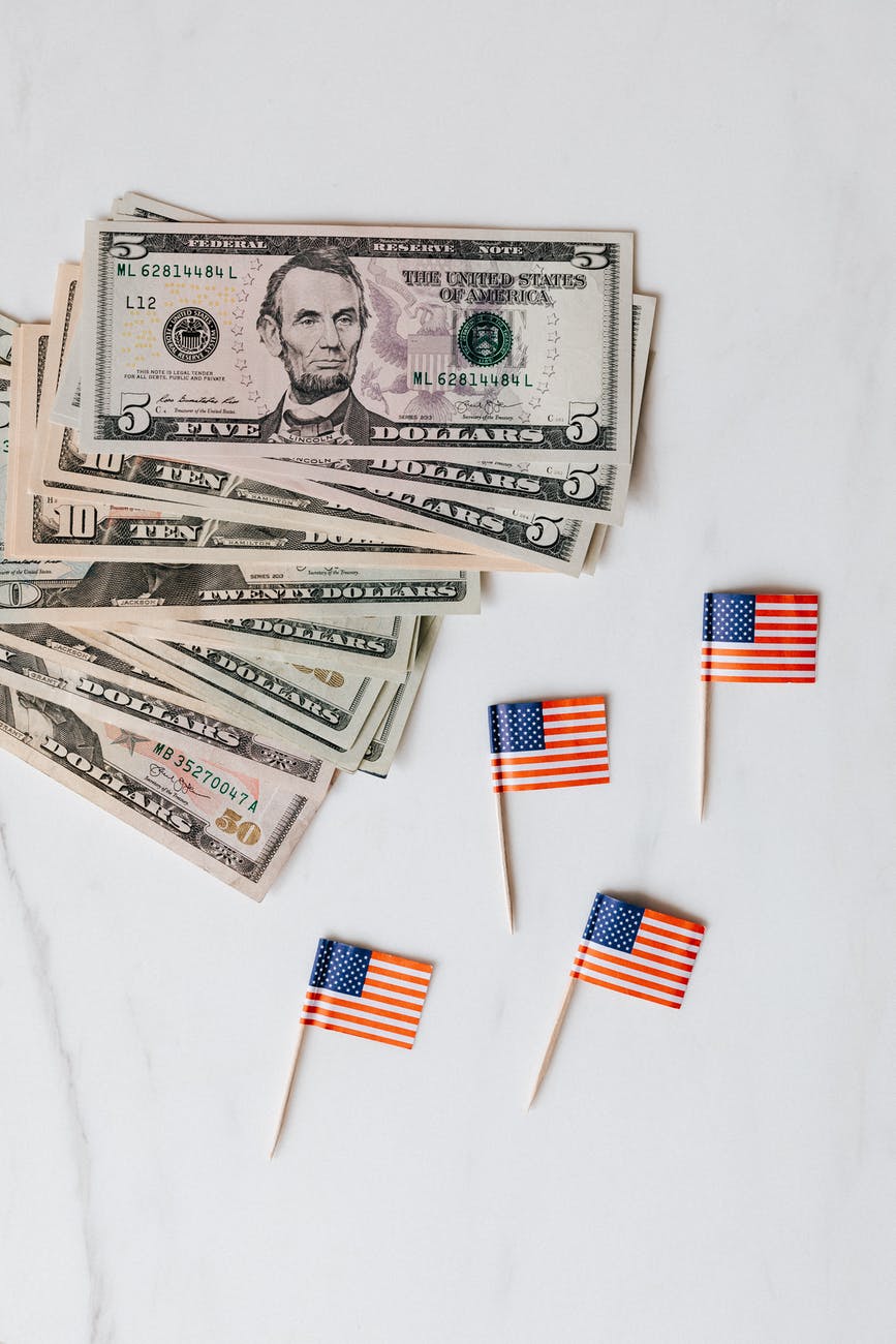 small paper usa flags placed on white surface with dollars