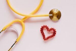 stethoscope near decorative coil tie in heart shape on pink surface