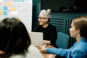 woman in black sweater and eyeglasses sitting on chair beside woman in blue shirt