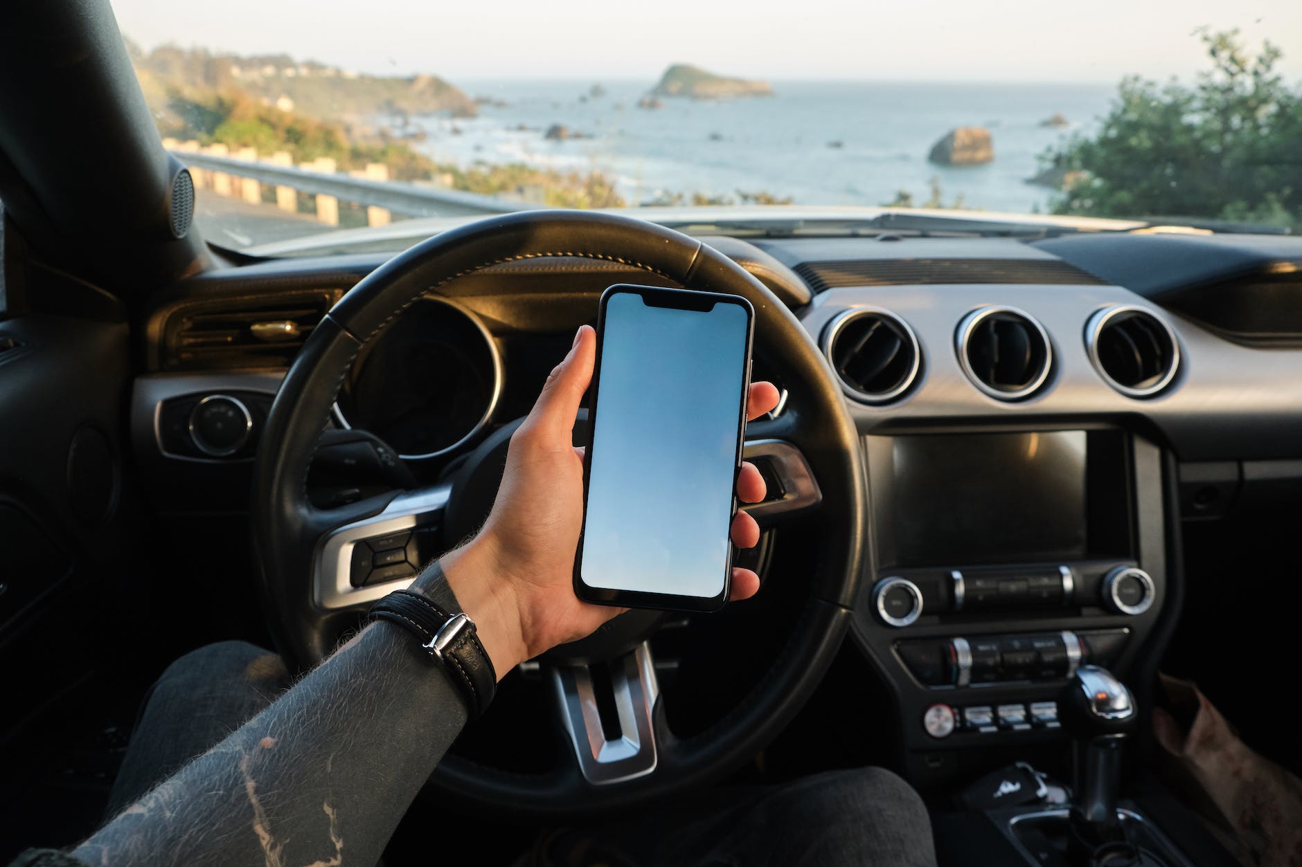 crop man using smartphone while sitting in car at seaside