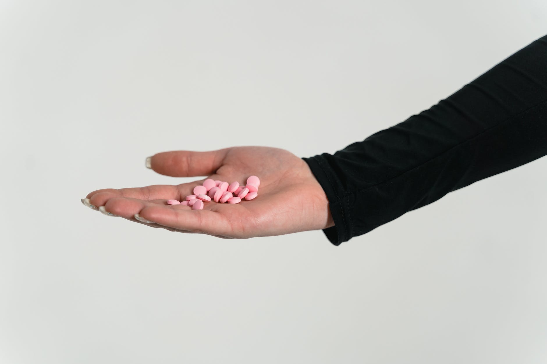 close up shot of a person holding pink pills on white background