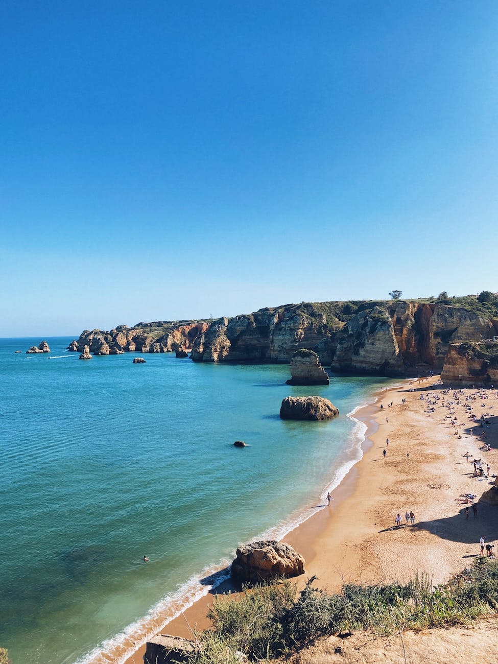 rock formations around sunlit beach on sea shore under clear sky