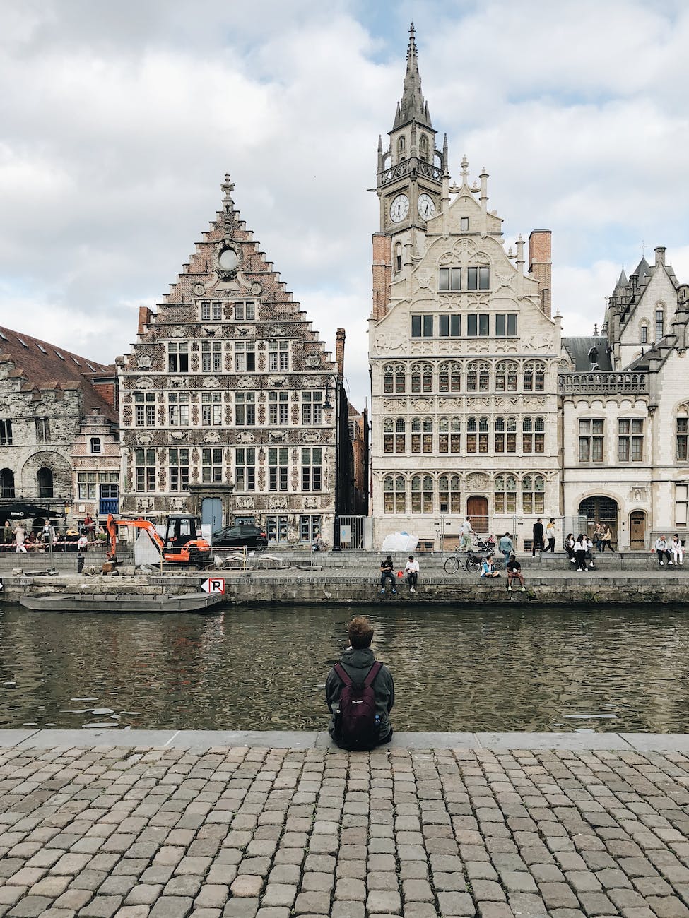 person sitting on pavement beside body of water