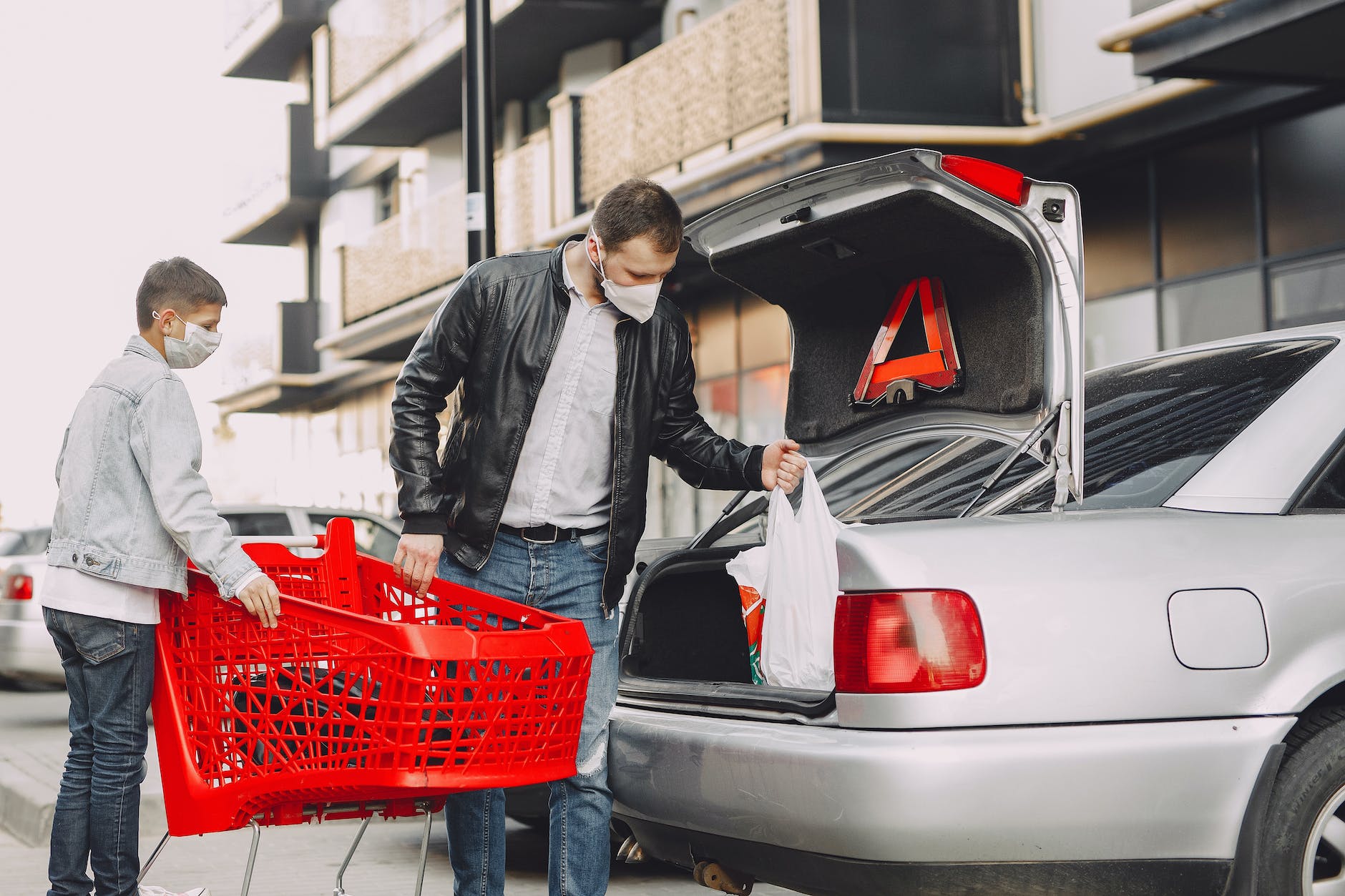 man and boy in protective masks putting shopping bag in trunk