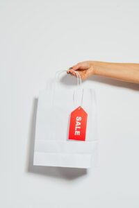 person holding a white paper bag with sale card