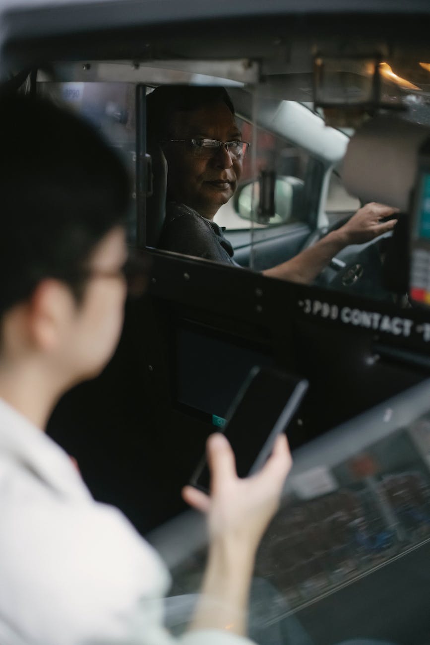 serious taxi driver looking through window on passenger with smartphone